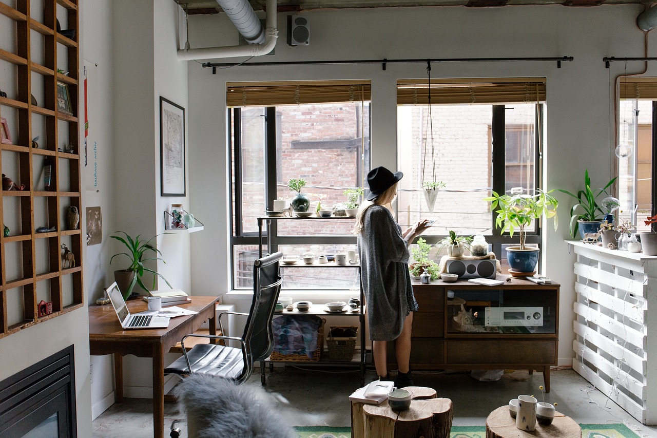 Woman tending to indoor plants in a cozy, modern apartment with a home office setup.