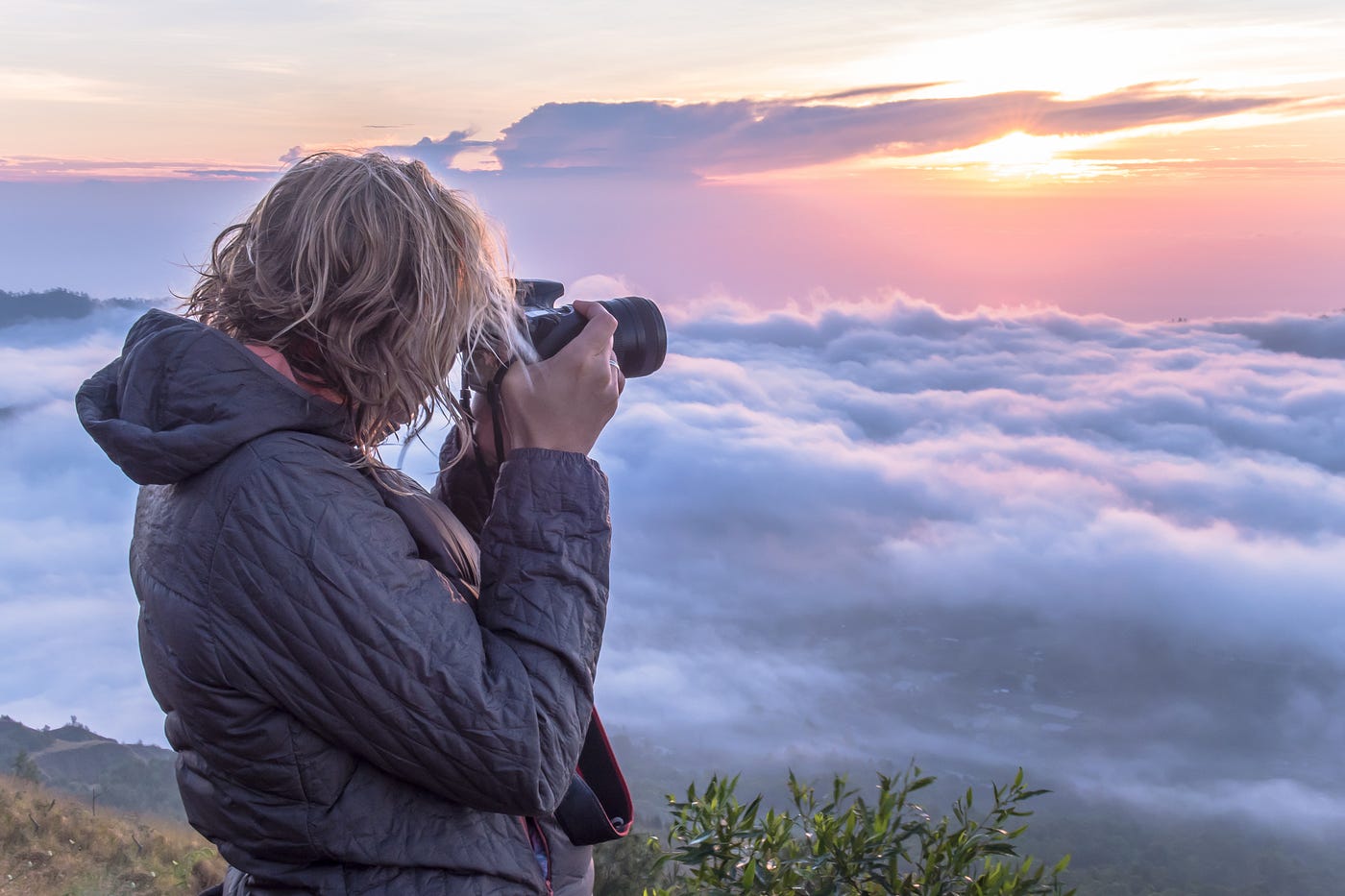 A photographer capturing a sunrise over a dramatic landscape of clouds and mountain peaks
