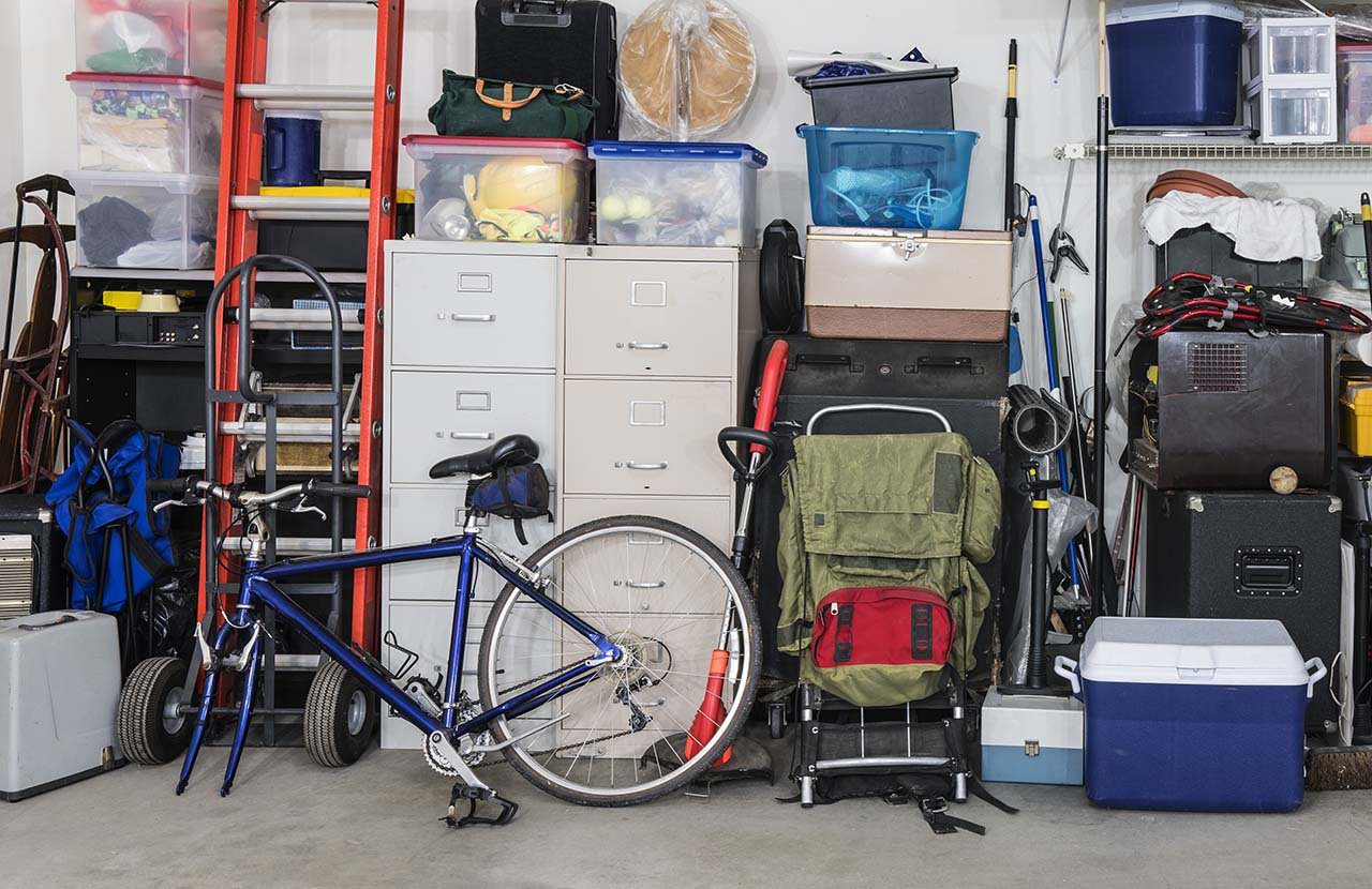 A cluttered home garage filled with household items like a bicycle, ladder, and bins available for rent