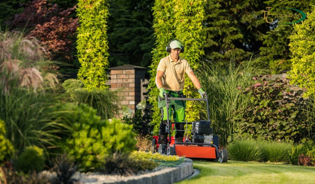 A landscaper in protective gear using a professional mower to groom a lush, green lawn in a garden